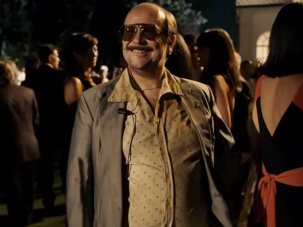 Santiago Segura caracterizado como José Luis Torrente sonríe con gafas de sol y traje desaliñado en una fiesta elegante nocturna, en un fotograma de 'Torrente, presidente'.