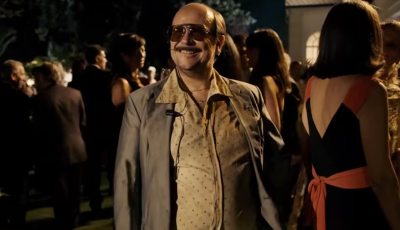 Santiago Segura caracterizado como José Luis Torrente sonríe con gafas de sol y traje desaliñado en una fiesta elegante nocturna, en un fotograma de 'Torrente, presidente'.